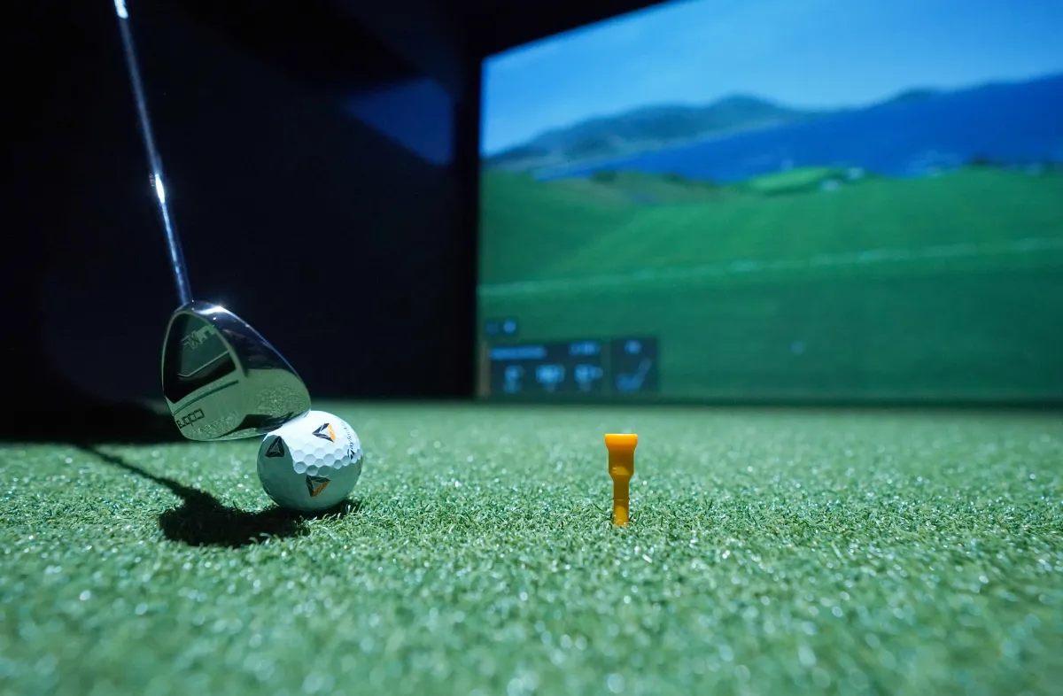 A golf club and ball on the turf in front of a Smash Sports simulator screen